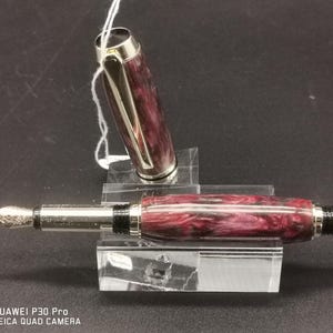 May include: A fountain pen with a burgundy and white marbled barrel and silver accents. The cap is off, revealing the nib. The pen is displayed on a clear acrylic stand. The pen is a writing instrument.