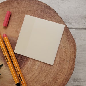 May include: A blank white note card on a wooden surface with two yellow pencils and a pink eraser.
