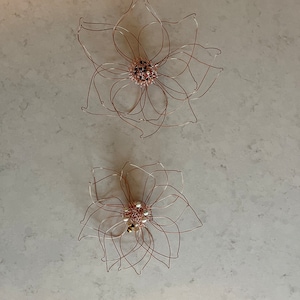 Op de afbeelding: Twee draadbeelden van bloemen met een parelmoercentrum. De bovenste bloem is groter en heeft een bruin centrum. De onderste bloem is kleiner en heeft een wit centrum met een kleine bij erop.