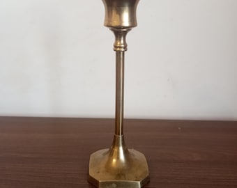 May include: A gold metal candle holder with a simple design. The holder has a round base and a tall, slender stem.