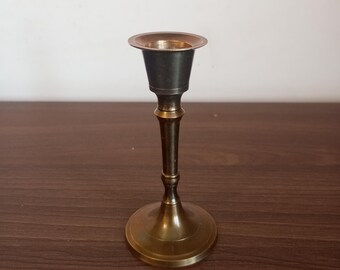 May include: A gold metal candle holder with a simple design. The holder has a round base and a tall, slender stem.