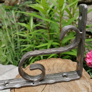 May include: A silver metal shelf bracket with a decorative scroll design. The bracket is mounted on a wooden surface.