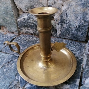 Peut inclure: Un chandelier en laiton vintage avec un motif de feuille décoratif et une poignée. Le chandelier a une base ronde et une tige cylindrique haute.