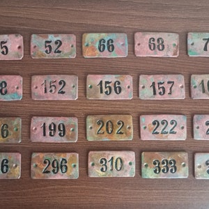 Puede incluir: Veinte etiquetas rectangulares de cobre con números negros. Los números van del 45 al 340.