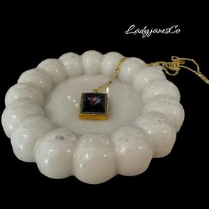 Può includere: Piatto portaoggetti in ceramica bianca con un design rialzato a forma di bolle. Una collana con catena dorata e un ciondolo quadrato riposa nel piatto. Il ciondolo contiene un'immagine in bianco e nero.