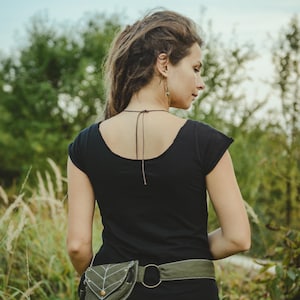 May include: A black short-sleeved top with a scoop neckline and a thin tie at the back of the neck. An olive green belt features a leaf-shaped pouch with white stitching, a metallic snap button, and a circular metal ring attachment at the waist.