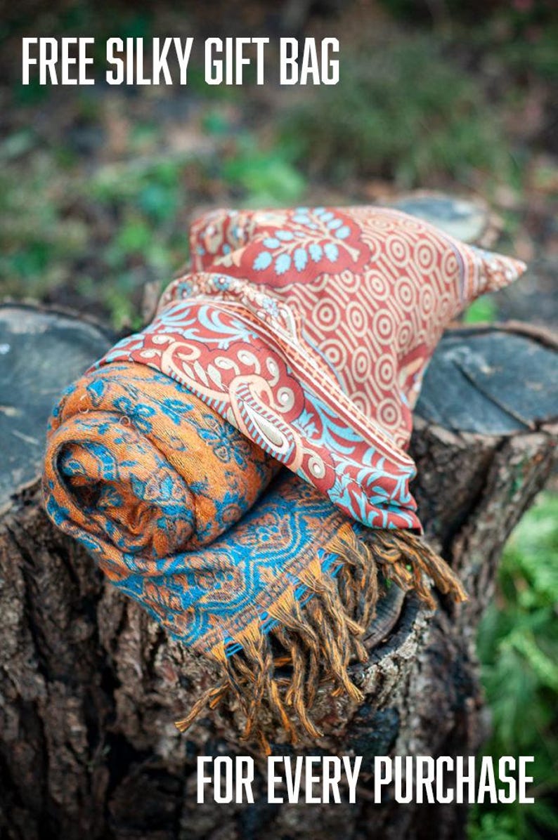 May include: A rolled scarf featuring a vibrant orange and blue floral pattern with a contrasting red and blue geometric border, finished with fringed edges. The text FREE SILKY GIFT BAG FOR EVERY PURCHASE is displayed in white at the top and bottom.