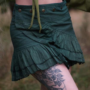 May include: A dark green wrap skirt with a ruffled hem and a row of buttons along the waistband.