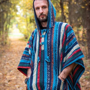 Könnte beinhalten: Ein Kapuzenponcho mit einem farbenfrohen Streifenmuster in Blau-, Rot- und Weißtönen. Der Poncho hat eine Vordertasche und einen Kordelzugverschluss. Das Kleidungsstück besteht aus einem dicken, gewebten Stoff, der für kühleres Wetter geeignet ist.