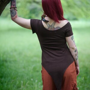 May include: A dark brown short-sleeved top with a wide scoop neckline and a long, pointed hemline that extends down the back, paired with loose-fitting, textured orange trousers featuring side pockets and side ties at the waist.