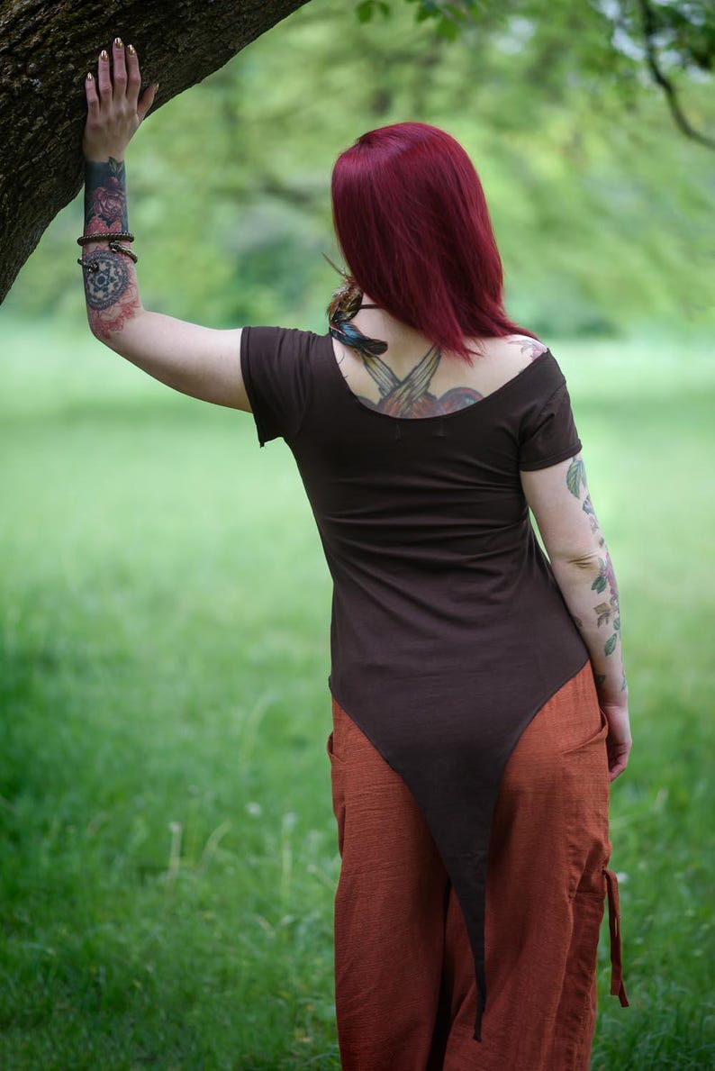May include: A dark brown short-sleeved top with a wide scoop neckline and a long, pointed hemline that extends down the back, paired with loose-fitting, textured orange trousers featuring side pockets and side ties at the waist.