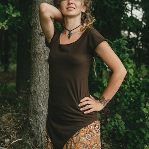 May include: A dark brown short-sleeved tunic with a high-low hemline paired with loose-fitting mustard yellow trousers featuring a white and brown floral pattern. The tunic has a scoop neckline and is worn with a black cord necklace with a pendant.