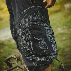 Könnte beinhalten: Schwarze Cargohose mit einem weißen geometrischen Muster und einer großen Tasche an der Seite. Die Hose hat einen Gürtel mit Metallschnallen.
