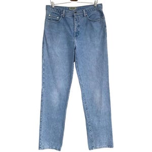 May include: Light blue denim jeans featuring a classic five-pocket design, a button fly closure, and a straight-leg cut. The fabric displays a faded wash with subtle white paint splatter details near the bottom hems, hanging on a wooden hanger.