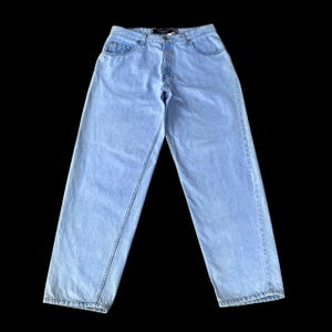 May include: Light blue denim jeans featuring a high-waisted fit, a classic five-pocket design, a metal button closure, and a zip fly. The fabric has a faded wash appearance with visible stitching along the seams and belt loops at the waistband.