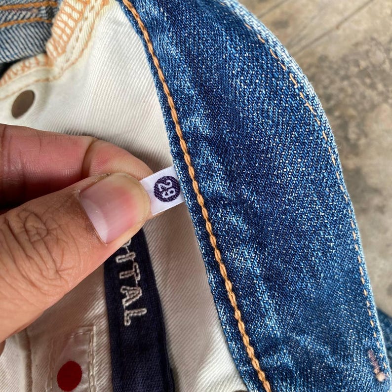 Puede incluir: Primer plano de unos vaqueros azules con una etiqueta de talla 29. Los vaqueros tienen un dise&ntilde;o cl&aacute;sico de cinco bolsillos, con costuras visibles y un lavado claro. La etiqueta es blanca con el n&uacute;mero 29 en un c&iacute;rculo negro.