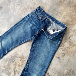 Puede incluir: Vaqueros azules de mezclilla con un dise&ntilde;o cl&aacute;sico de cinco bolsillos. Los vaqueros est&aacute;n ligeramente descoloridos, con cierre de bot&oacute;n y cremallera. Los vaqueros est&aacute;n colocados sobre una superficie de hormig&oacute;n.
