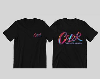 May include: Two black t-shirts displayed side-by-side. The left shirt features a small, colorful, gradient-style logo on the chest that reads "COLOR CUSTOM PRINTS." The right shirt displays the same logo in a much larger size across the back.