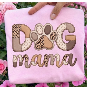 May include: A light pink sweatshirt with the words "DOG mama" in a patchwork design. The letters and paw print are in shades of brown and tan with a leopard print pattern.