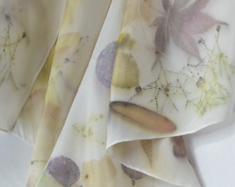 May include: A white silk scarf with a delicate pattern of leaves and flowers in shades of brown, yellow, and purple. The scarf is folded in a way that shows the intricate details of the design.