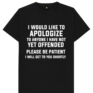 Op de afbeelding: Zwart T-shirt met witte tekst die luidt: "Ik wil me verontschuldigen bij iedereen die ik nog niet heb beledigd. Wees geduldig. Ik kom zo snel mogelijk bij je terug."