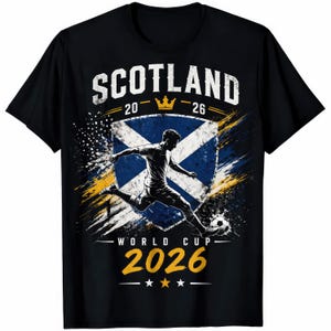 May include: Black t-shirt featuring a soccer player kicking a ball, with the text "SCOTLAND" above a shield with the Scottish flag. The shirt also displays "WORLD CUP 2026" and the years "20-26".