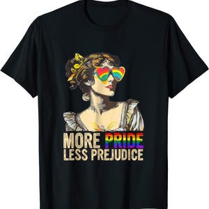 Może przedstawiać: Czarna koszulka z ilustracją w stylu vintage kobiety w tęczowych okularach przeciwsłonecznych w kształcie serca. Tekst "MORE PRIDE LESS PREJUDICE" jest wyświetlany w tęczowych kolorach. Wyraz dumy LGBTQ+.