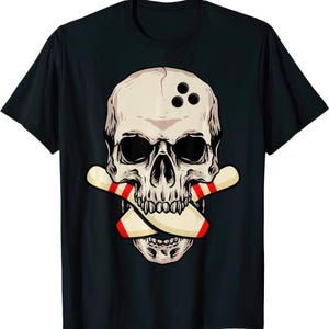 May include: Black t-shirt featuring a skull with three bowling ball holes and crossed bowling pins. The skull is off-white with black eye sockets and a detailed jawline. The bowling pins are beige with red stripes.