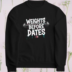 May include: Black sweatshirt with the text "WEIGHTS BEFORE DATES" in white, with a barbell graphic. The text has a splatter effect with teal and red accents. A fitness-themed apparel item.