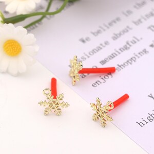 May include: Three gold snowflake charms with red stems. The charms are on a white surface with text that reads "We believe in the passionate about their craft and meaningful. Enjoy shopping with us."