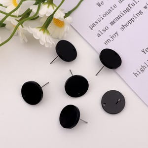 May include: Six black round earring blanks with a silver post. The earring blanks are on a white surface.