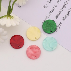 May include: Five round, flat, decorative pieces with a hole in the center. The pieces are made of a marbled material and are in the colors red, yellow, green, blue, and pink.