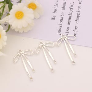 Puede incluir: Tres abalorios de metal plateado en forma de lazo con un diseño sencillo. Los abalorios son perfectos para añadir un toque de elegancia a los proyectos de joyería.