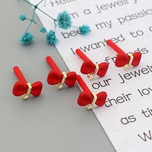 May include: Four red bow charms with gold accents. The charms are on a white surface with text.