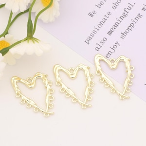 May include: Three gold heart-shaped metal charms with decorative details and multiple jump rings. The charms are on a white surface.