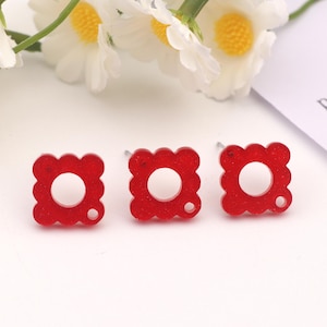 Pode incluir: Três brincos quadrados vermelhos com glitter e um círculo recortado no centro. Cada brinco tem um pequeno furo na lateral para prender um poste.