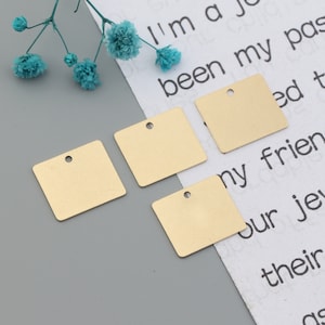 May include: Four gold square metal tags with a hole at the top. The tags are on a white surface with text.