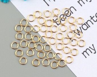 May include: A large quantity of small, gold-colored jump rings. The rings are arranged in a loose pile on a white surface.