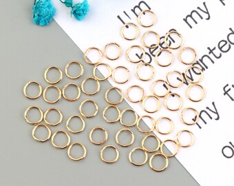 May include: A close-up of a group of gold jump rings. The rings are scattered on a white surface with text.