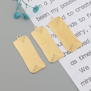 May include: Three gold-colored metal rectangular pendant charms with a textured, concentric circle design. Each charm has a small loop at the top for attaching to a necklace or bracelet.