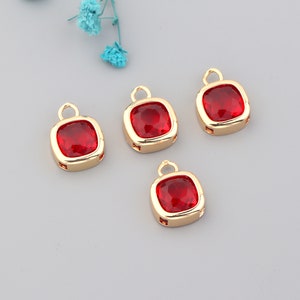 May include: Four gold-toned charms with red square-shaped glass stones. Each charm has a loop at the top for attaching to a necklace or bracelet.
