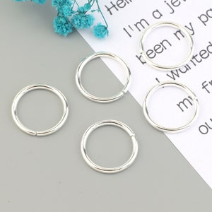May include: Four silver jump rings, each with a diameter of approximately 1 inch. The rings are smooth and shiny, and they are perfect for jewelry making or other crafting projects.