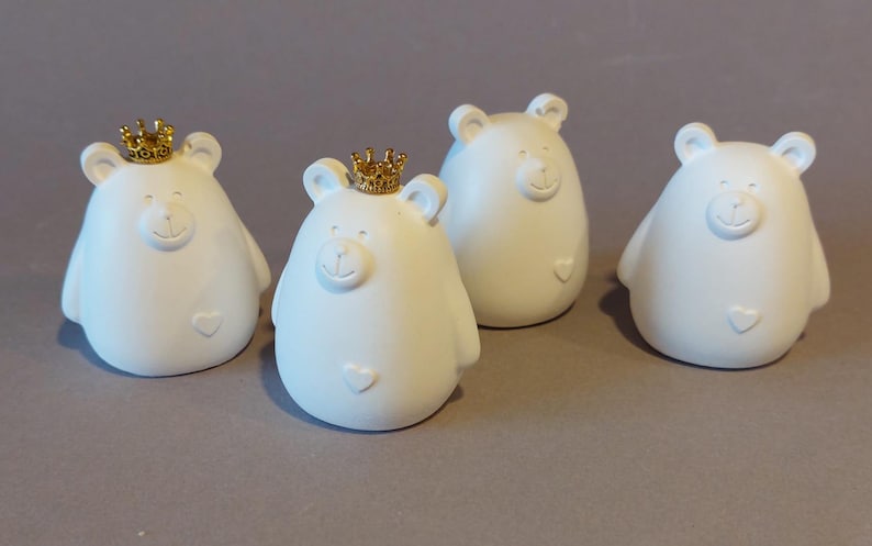 Könnte beinhalten: Vier weiße Keramik-Bärenfiguren mit goldenen Kronen. Jeder Bär hat ein Herz auf der Brust.