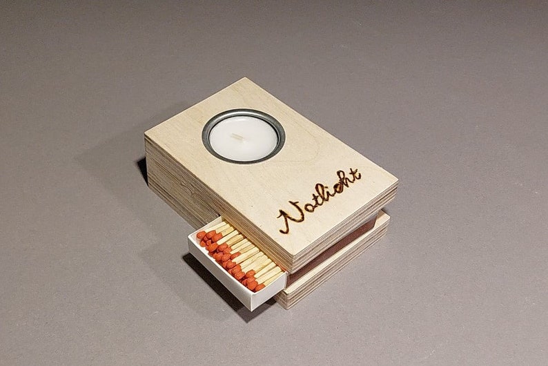 Könnte beinhalten: Eine Holzkiste mit einem kleinen Kerzenhalter und einer Schublade, die Streichhölzer enthält. Die Kiste ist mit "Natlicht" beschriftet.