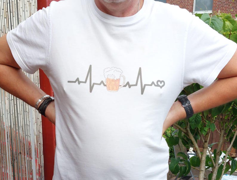 Könnte beinhalten: Weißes T-Shirt mit einem Bier-Motiv. Eine graue Herzschlaglinie enthält einen Bierkrug mit Schaum und einem Herz. Der Bierkrug ist mit einer hellen, bernsteinfarbenen Flüssigkeit und weißem Schaum gefüllt.