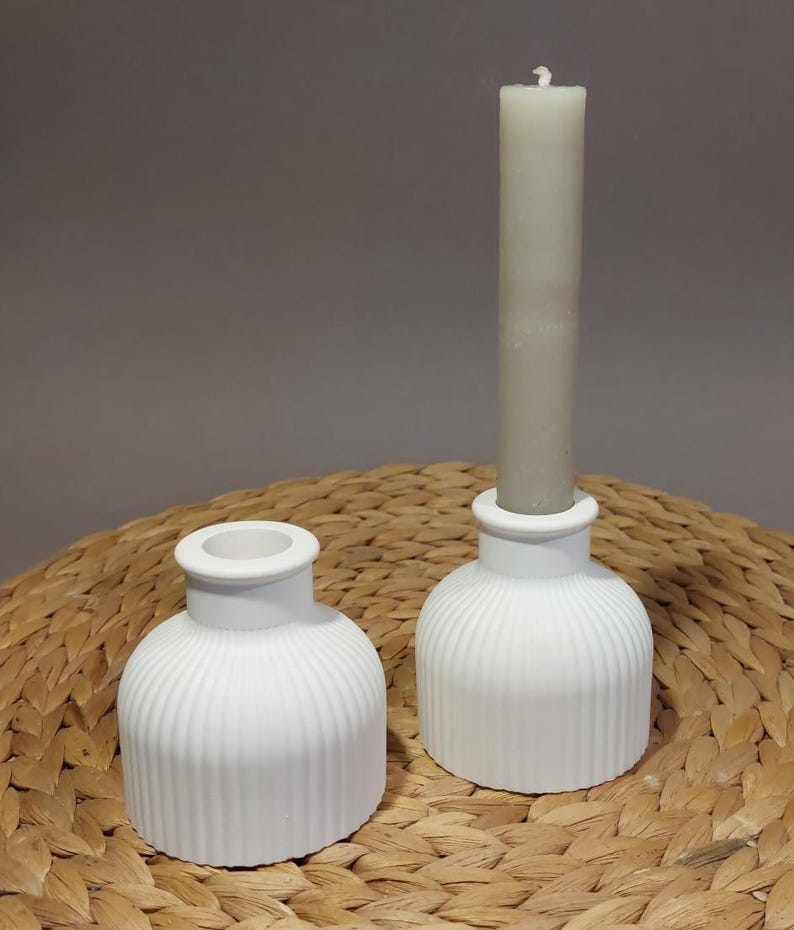 Könnte beinhalten: Zwei weiße Kerzenhalter aus Keramik mit geripptem Design. Der Halter rechts hat eine weiße Kerze drin.