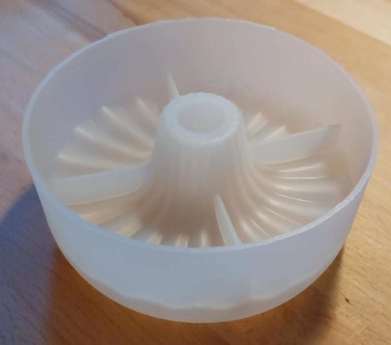 Könnte beinhalten: Ein weißer Zitruspresser aus Kunststoff mit einem zentralen Kegel und einer umgebenden Schüssel. Der Entsafter hat eine geriffelte Innenseite und ist zum Auspressen von Saft aus Zitrusfrüchten bestimmt. Die Schüssel hat einen Durchmesser von etwa 15 cm.