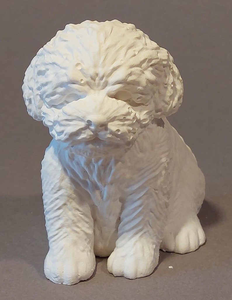 Könnte beinhalten: Eine weiße, strukturierte Skulptur eines sitzenden Welpen. Der Welpe hat ein flauschiges, strukturiertes Fell und sitzt mit seinen Vorderpfoten nach vorne. Die Skulptur besteht aus einem festen, undurchsichtigen Material.