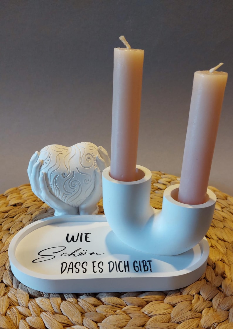 Könnte beinhalten: Weißer Kerzenhalter aus Keramik mit zwei Händen, die ein Herz halten, und dem Text "Wie schön dass es dich gibt".
