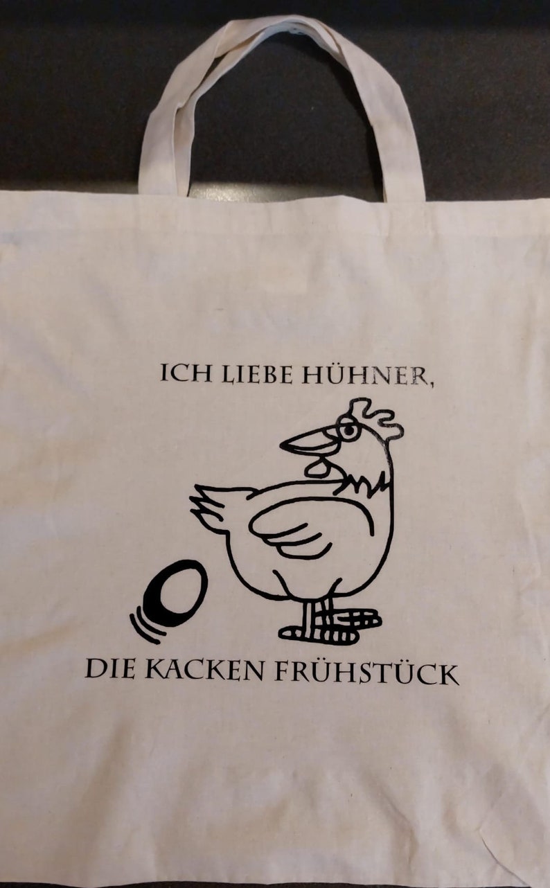 Könnte beinhalten: Eine weiße Einkaufstasche mit schwarzem Text und einem Comic-Huhn. Der Text lautet "Ich liebe Hühner, die kacken Frühstück".